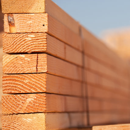LumberStack of neatly arranged, light brown wooden planks lined vertically, showing natural wood grain and textures, under soft, warm daylight.